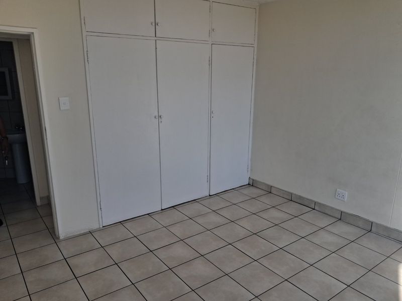 An empty bedroom featuring neutral tiled flooring and white built-in cupboards with overhead storage compartments.