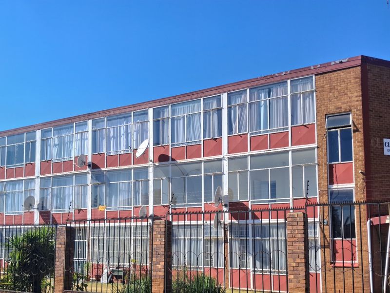 Front elevation of the Clematis apartment building featuring a brick facade, extensive glass window panels, and perimeter security fencing with electric wire.