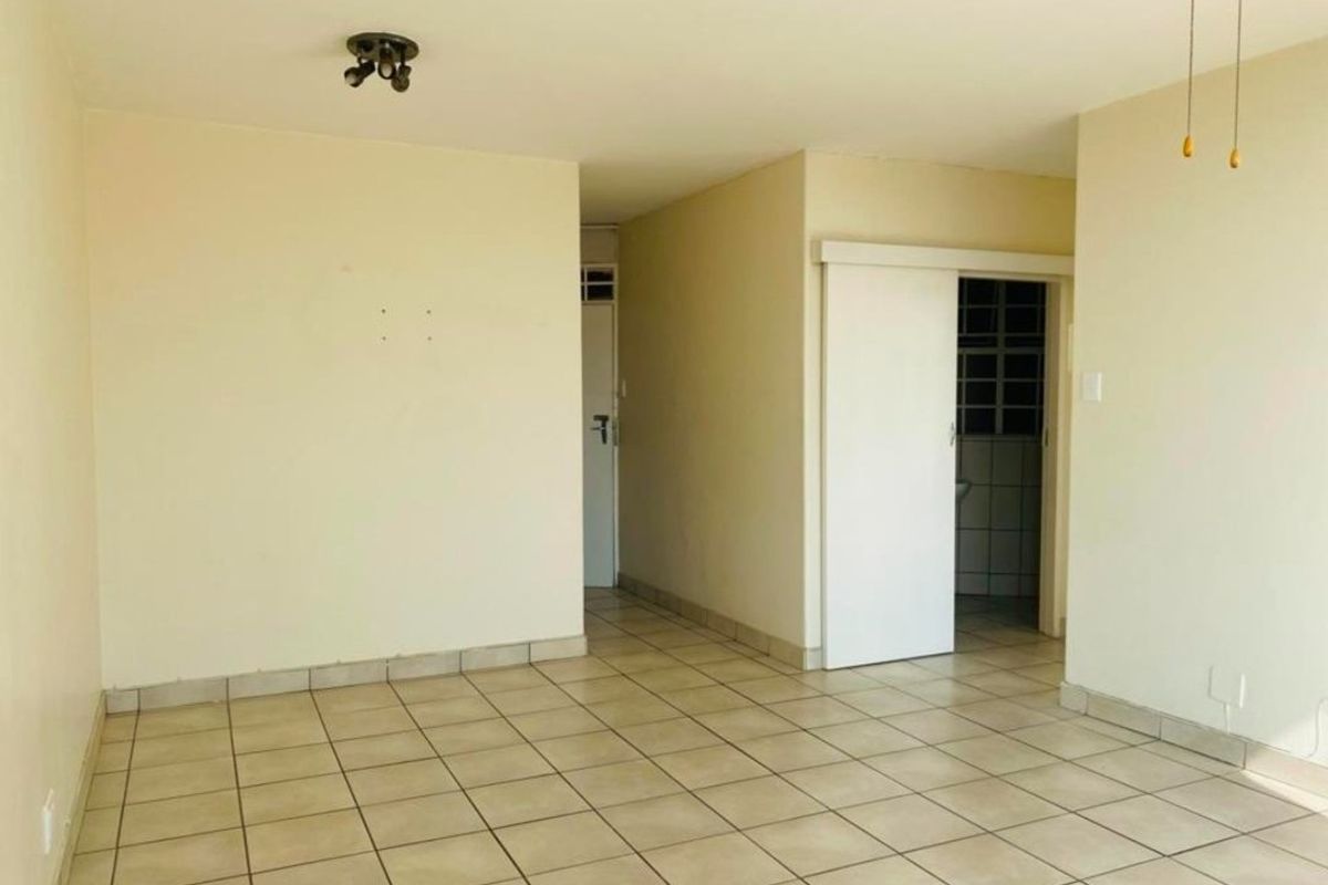 An empty living area featuring neutral tiled flooring and a sliding door, providing a blank canvas for interior design and personalization.