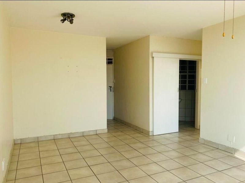 An empty living area featuring neutral tiled flooring and a sliding door, providing a blank canvas for interior design and personalization.