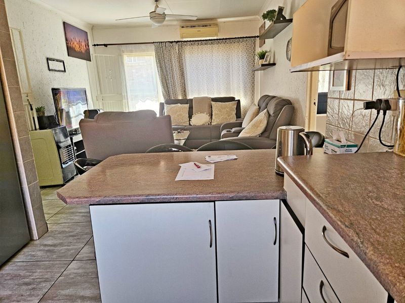Open-plan living area featuring a functional kitchen with laminate countertops, tiled flooring, and a ceiling fan, seamlessly flowing into the adjacent lounge space.