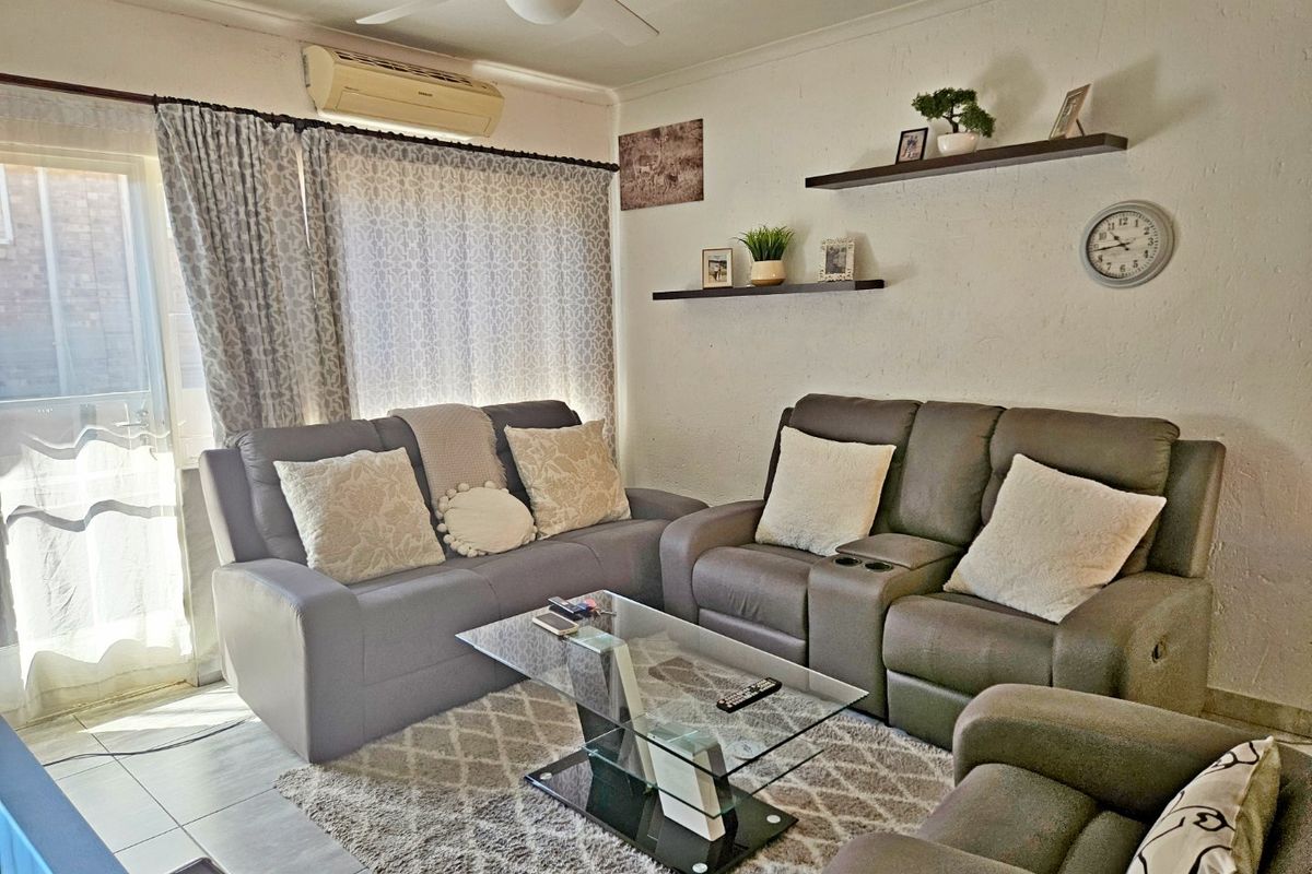 A comfortable living room featuring tiled flooring, a ceiling fan, and a wall-mounted air conditioning unit with access to an outdoor area.