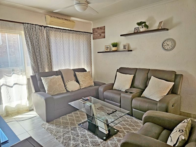 A comfortable living room featuring tiled flooring, a ceiling fan, and a wall-mounted air conditioning unit with access to an outdoor area.