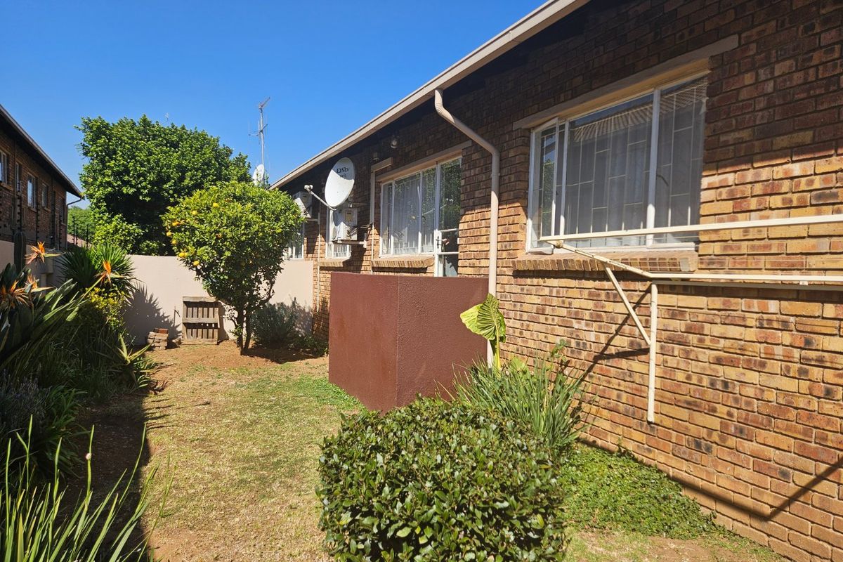 Rear exterior view of the townhouse featuring a brick facade, security window bars, and a wall-mounted washing line overlooking a private garden area.