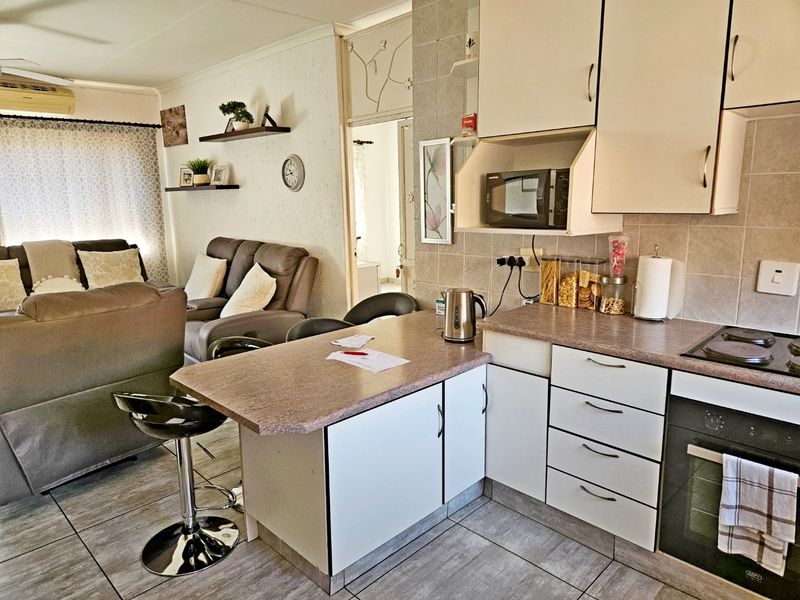 Open-plan living area featuring a functional kitchen with built-in cabinetry, oven, and hob, seamlessly flowing into the adjacent living space with tiled flooring.