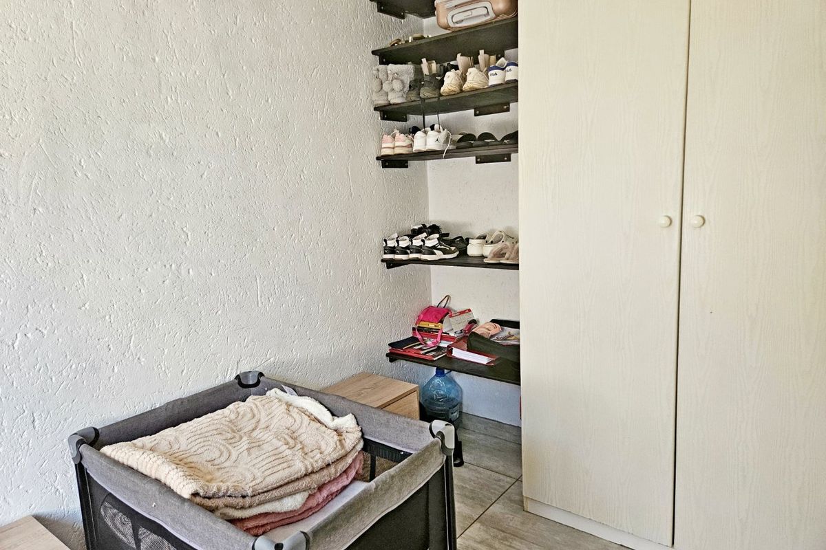 A bedroom featuring a built-in wardrobe and open wall-mounted shelving, finished with tiled flooring.