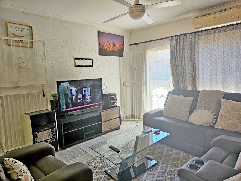 A comfortable living room featuring tiled flooring, a ceiling fan, and a wall-mounted air conditioning unit, with direct access to an outdoor area.