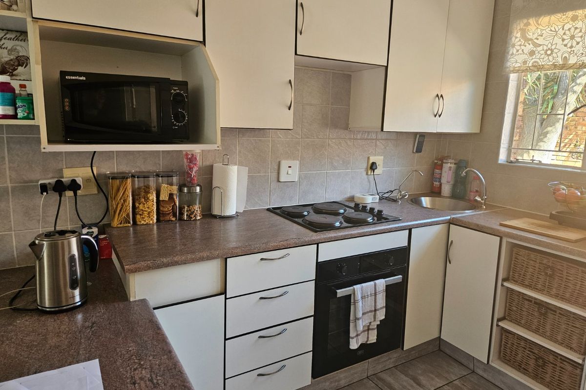 A functional kitchen featuring white cabinetry, laminate countertops, a built-in oven with electric hob, and tiled finishes throughout.