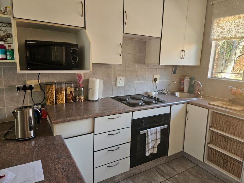 A functional kitchen featuring white cabinetry, laminate countertops, a built-in oven with electric hob, and tiled finishes throughout.