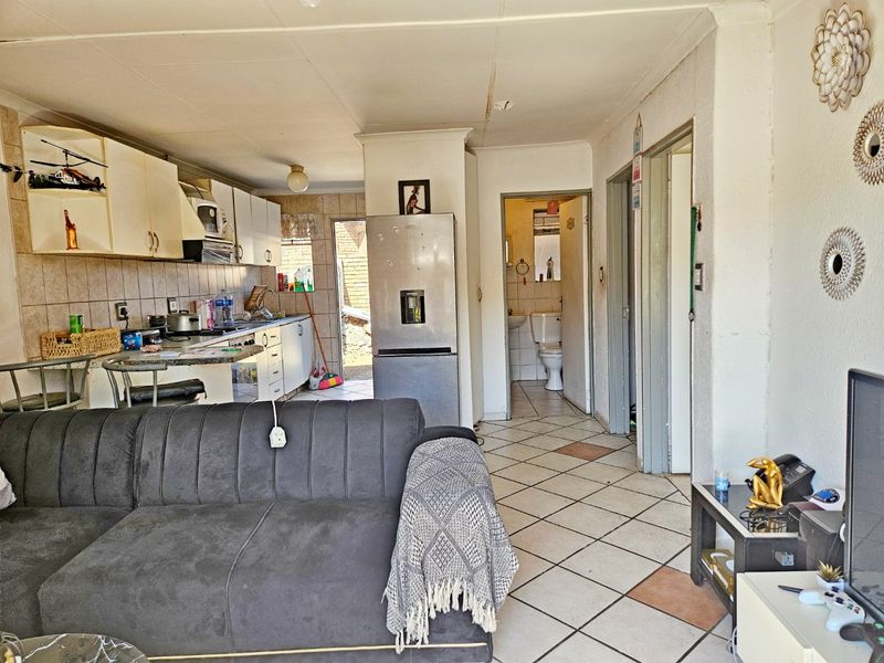 Open-plan living and kitchen area featuring tiled flooring and built-in cabinetry, with direct access to a bathroom and rear exterior space.