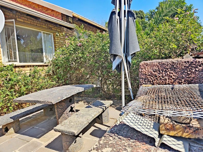 Outdoor patio area featuring a built-in brick braai, paved flooring, and direct access to the garden and townhouse exterior.