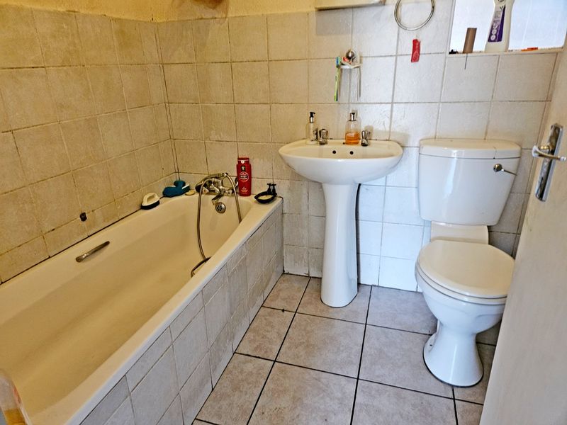 A dated bathroom featuring a standard bathtub, pedestal basin, and toilet with tiled walls and flooring, requiring cosmetic updates and maintenance.