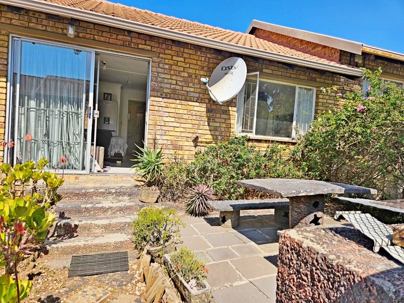 Rear exterior view of a face brick townhouse featuring a paved patio area, concrete steps, and a sliding glass door entrance.