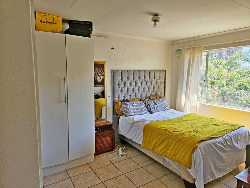 A bedroom featuring tiled flooring, a built-in wardrobe, and a large window providing natural light and garden views.