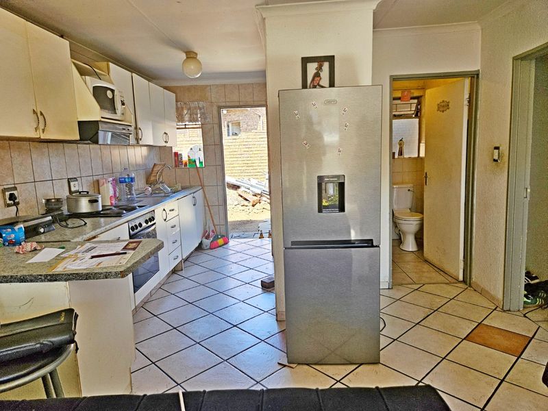 Functional kitchen featuring tiled flooring, built-in cabinetry, and a tiled backsplash, with direct access to the rear exterior and an adjacent bathroom.