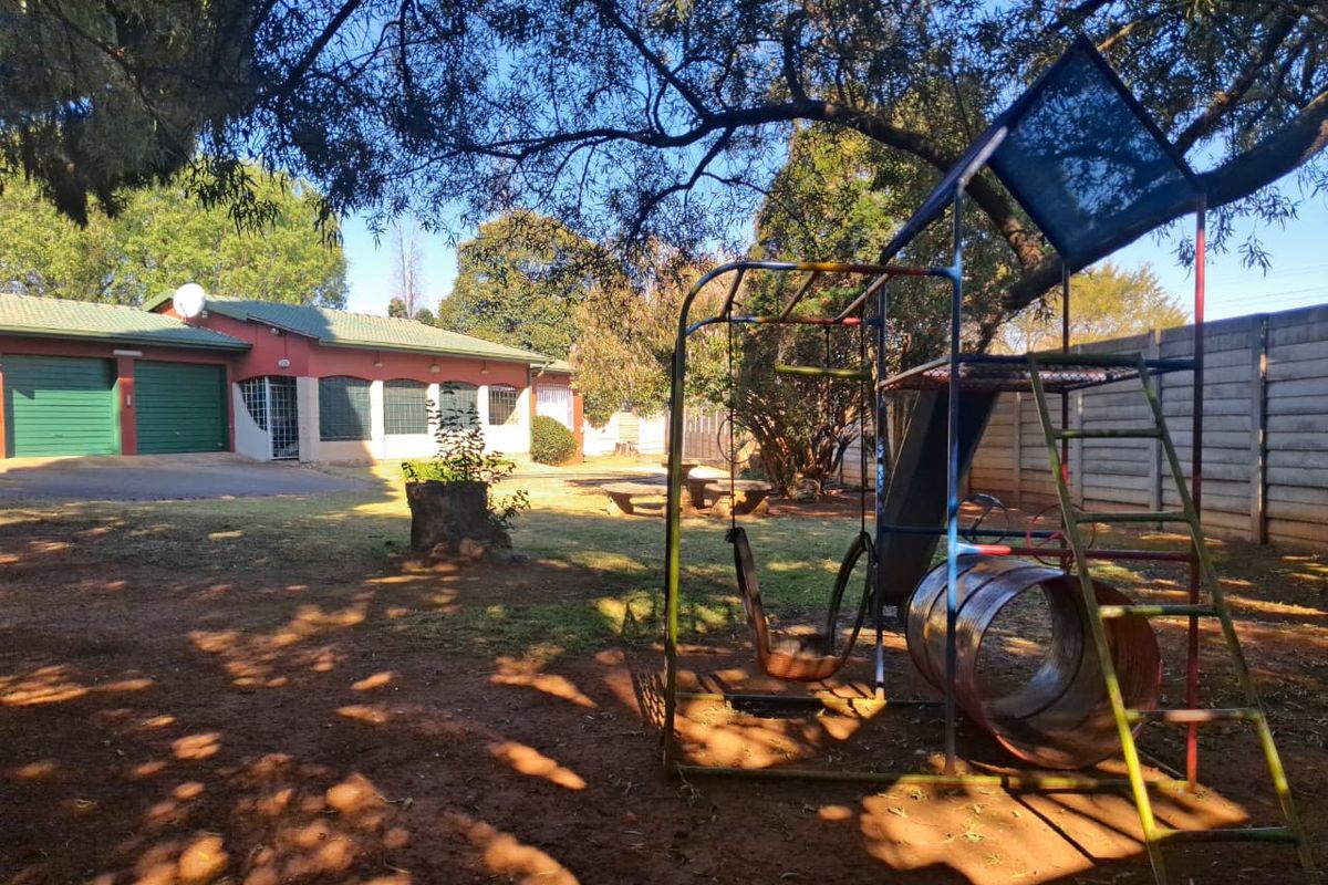 Spacious rear garden area featuring a double garage, concrete boundary walling, and mature trees, providing a functional outdoor space.