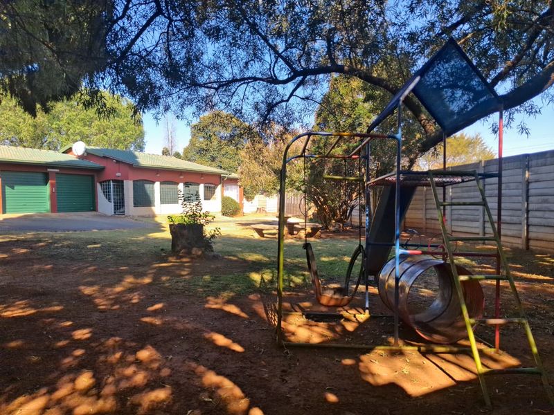 Spacious rear garden area featuring a double garage, concrete boundary walling, and mature trees, providing a functional outdoor space.