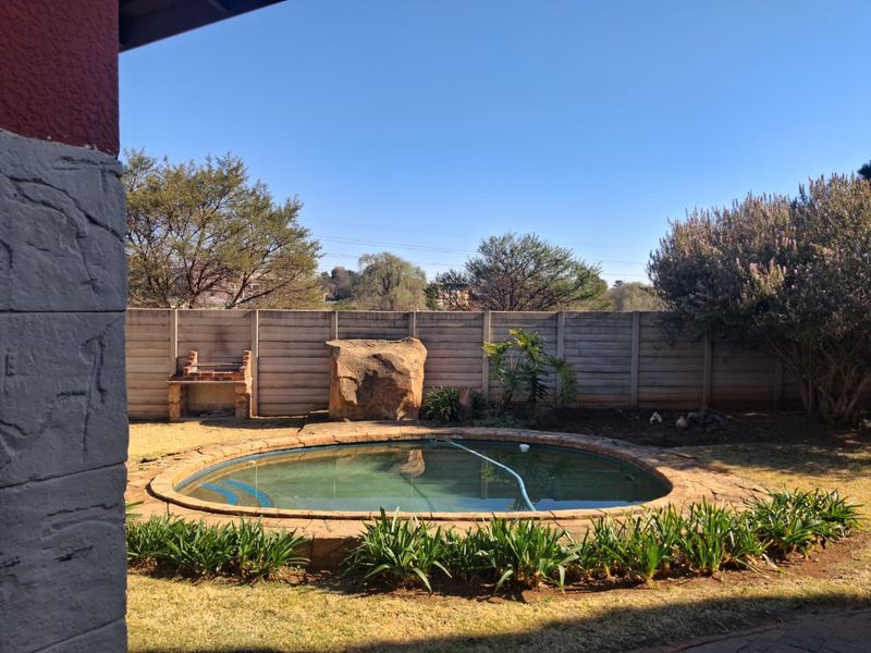 A backyard area featuring a circular swimming pool with stone coping, a built-in brick braai, and a precast concrete boundary wall.