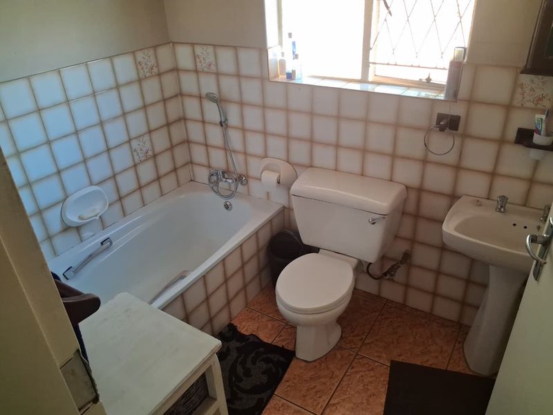 A compact bathroom featuring a bathtub, pedestal basin, and toilet with dated wall and floor tiling.