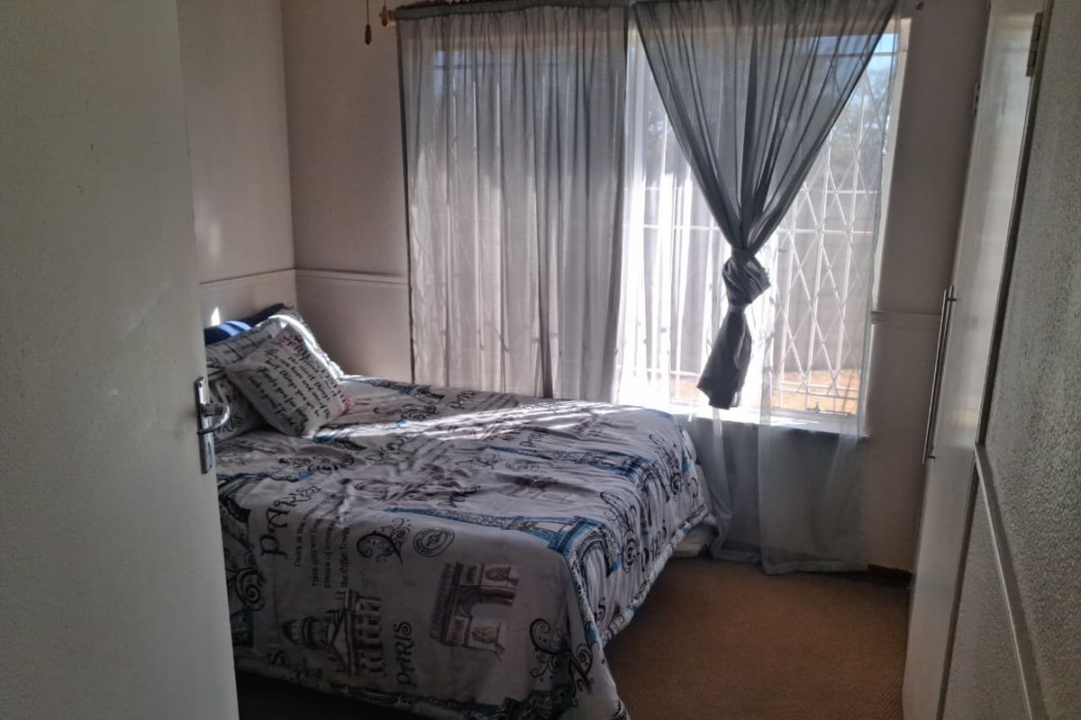 A functional bedroom featuring carpet flooring, a built-in wardrobe, and a window fitted with a security gate.