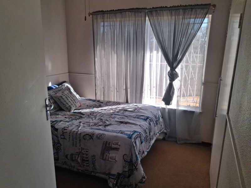 A functional bedroom featuring carpet flooring, a built-in wardrobe, and a window fitted with a security gate.