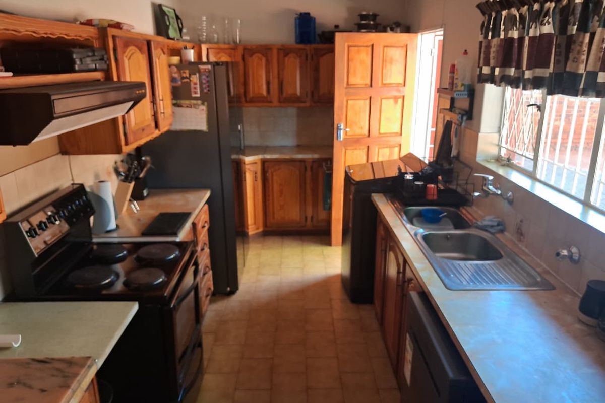 A functional kitchen featuring wooden cabinetry, laminate countertops, a double stainless steel sink, and an electric stove with an extractor fan.