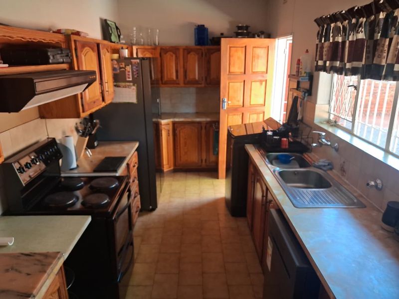 A functional kitchen featuring wooden cabinetry, laminate countertops, a double stainless steel sink, and an electric stove with an extractor fan.