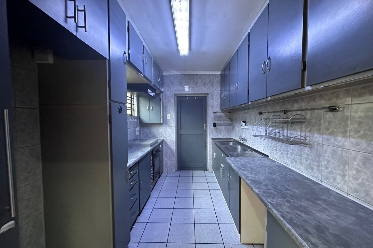 A galley-style kitchen featuring extensive built-in cabinetry, laminate countertops, a double sink, and tiled surfaces throughout, offering a functional layout ready for modernization.