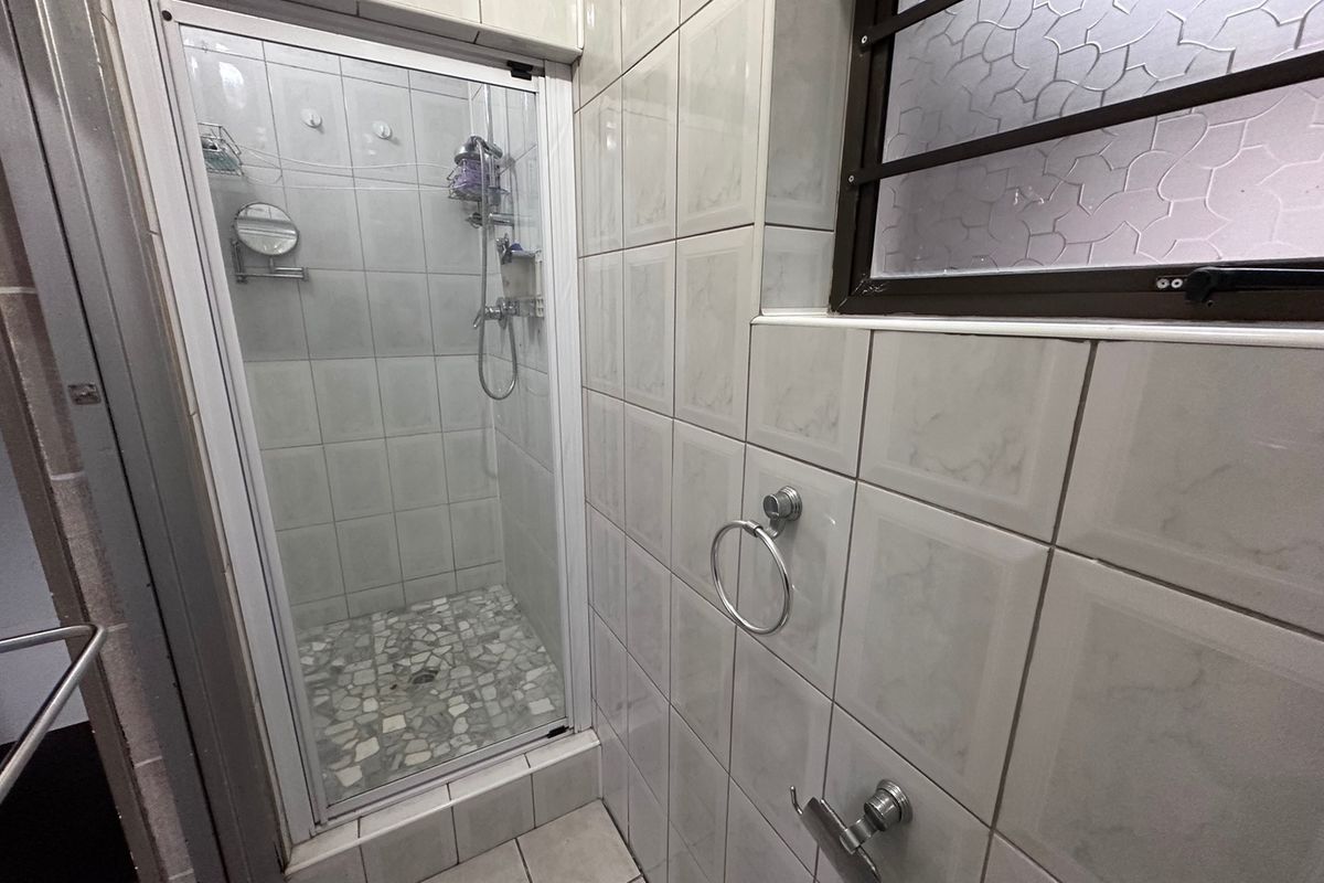 A functional bathroom featuring a tiled shower enclosure, wall-mounted towel hardware, and an obscured glass window with security bars.