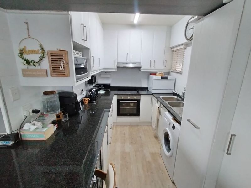 Compact kitchen featuring white cabinetry, dark granite countertops, built-in oven and hob, extractor fan, and integrated laundry plumbing.