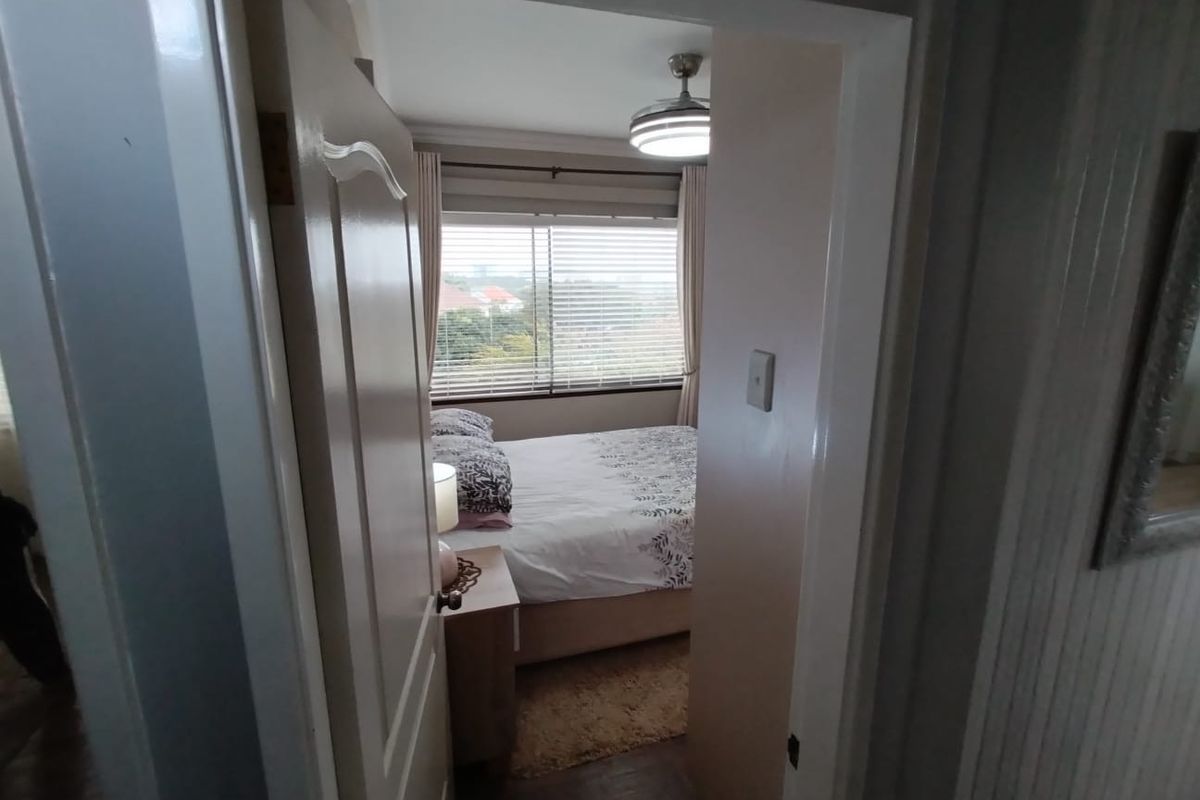 A view through a doorway into a bedroom featuring a ceiling fan and window with venetian blinds.