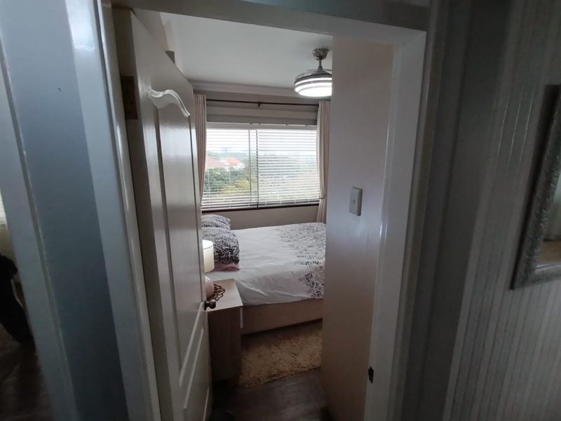 A view through a doorway into a bedroom featuring a ceiling fan and window with venetian blinds.