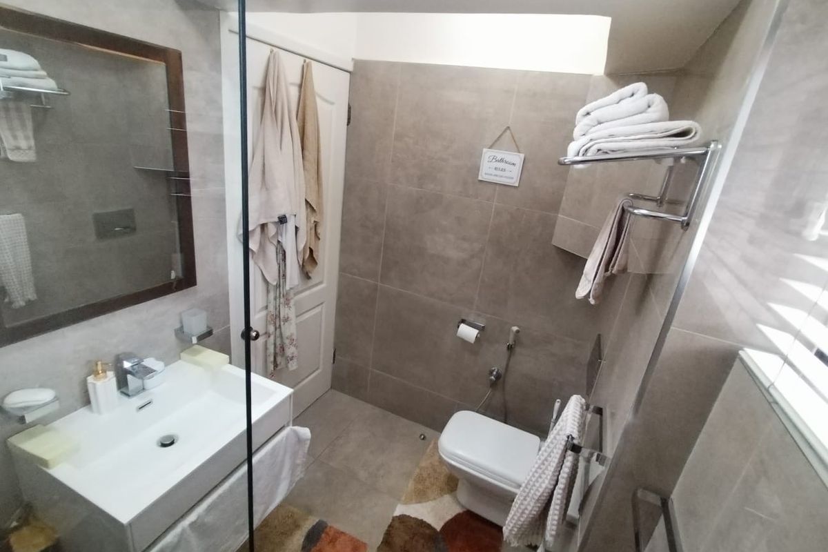 A modern, well-maintained bathroom featuring neutral-toned wall and floor tiles, a wall-mounted vanity with a basin, and a glass shower screen.