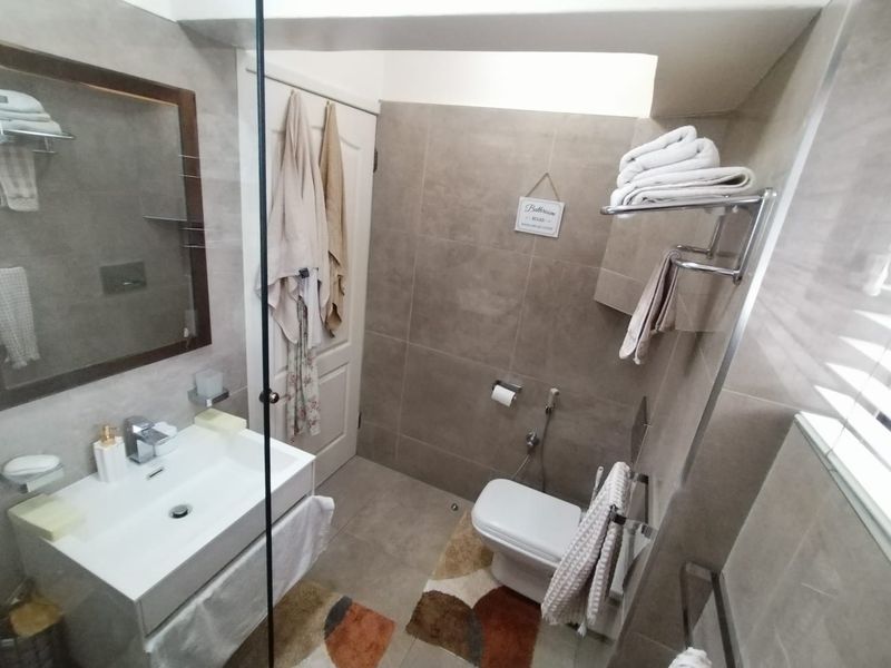 A modern, well-maintained bathroom featuring neutral-toned wall and floor tiles, a wall-mounted vanity with a basin, and a glass shower screen.