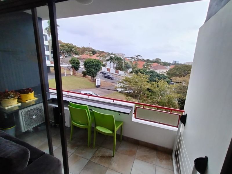 A covered balcony featuring tiled flooring, a built-in counter, and a metal balustrade, offering an elevated view of the surrounding neighborhood.