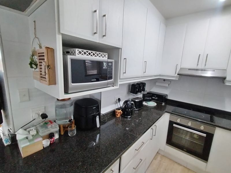 A functional kitchen featuring white cabinetry, dark granite countertops, and integrated appliances including an oven, hob, and extractor fan.