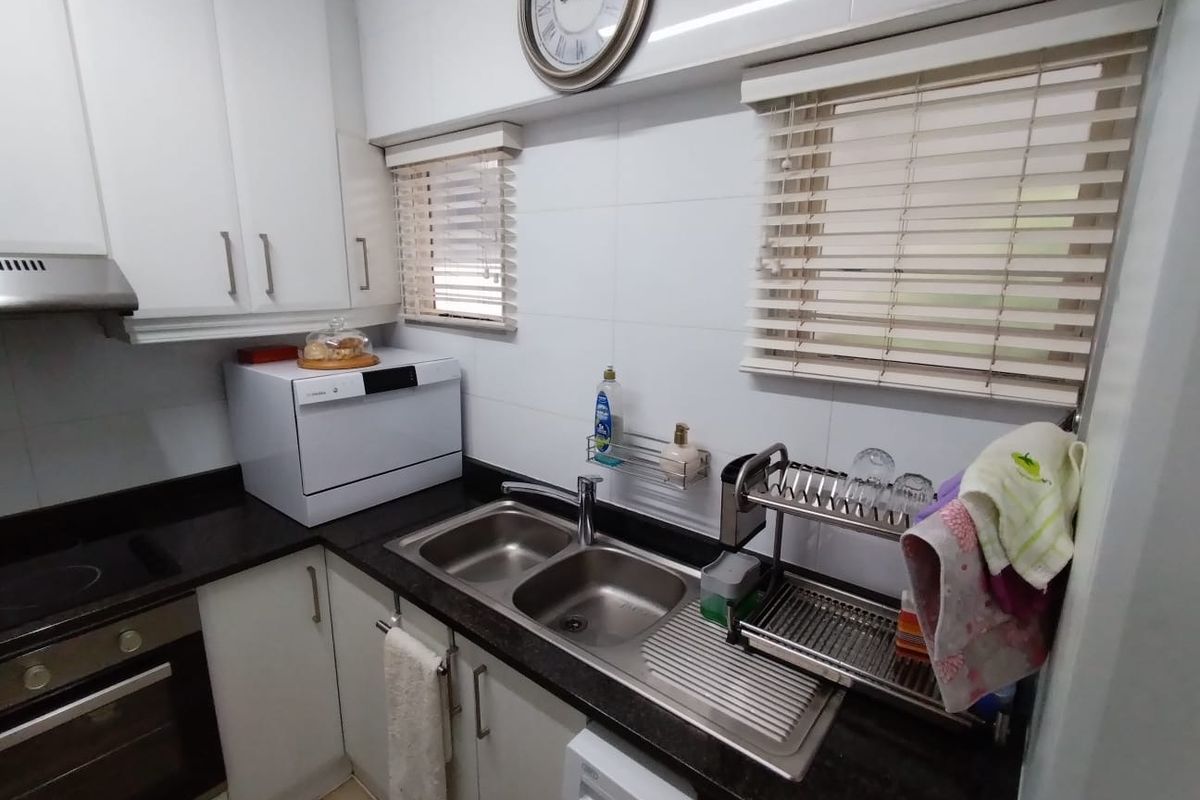 A compact, well-maintained kitchen featuring white cabinetry, dark granite countertops, a double stainless steel sink, and integrated cooking appliances.