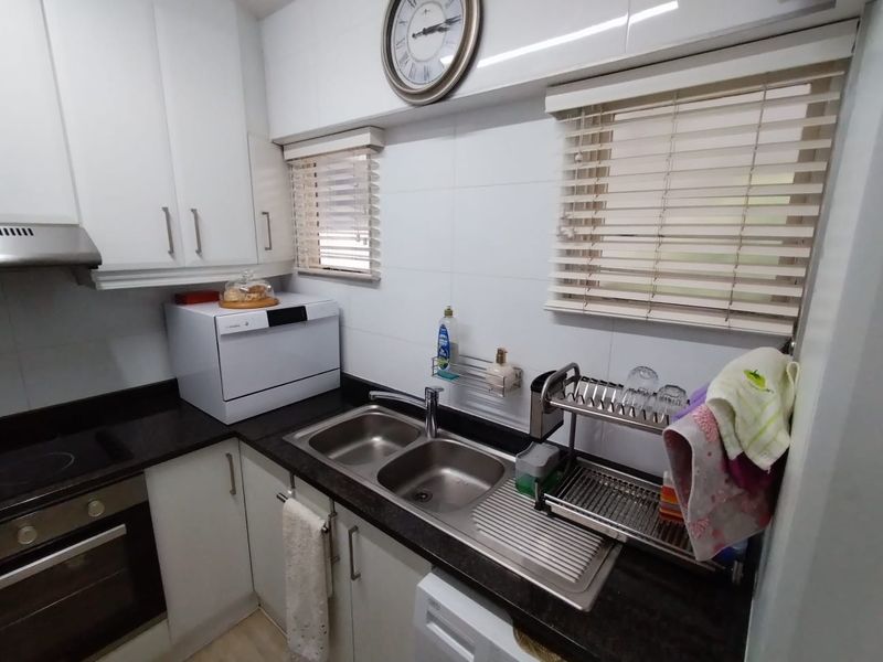 A compact, well-maintained kitchen featuring white cabinetry, dark granite countertops, a double stainless steel sink, and integrated cooking appliances.
