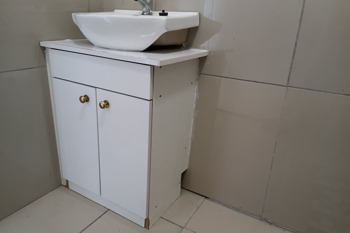 A bathroom vanity unit featuring a white cabinet and ceramic basin, set against tiled walls and flooring, requiring minor finishing work.