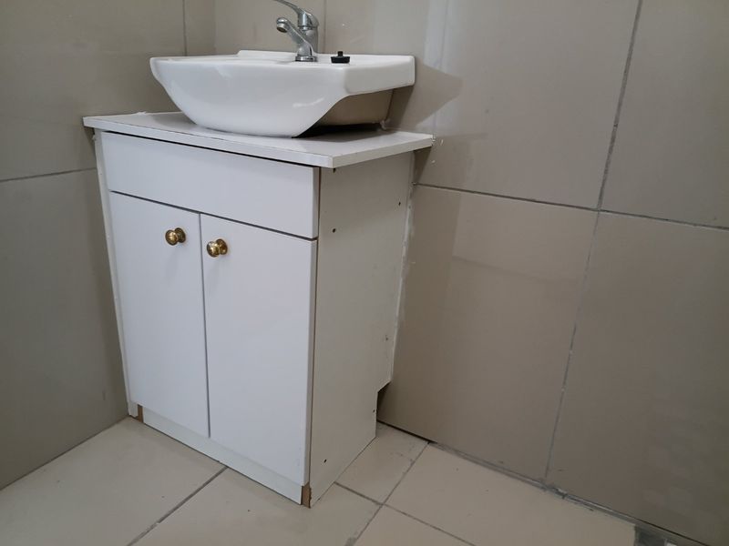 A bathroom vanity unit featuring a white cabinet and ceramic basin, set against tiled walls and flooring, requiring minor finishing work.
