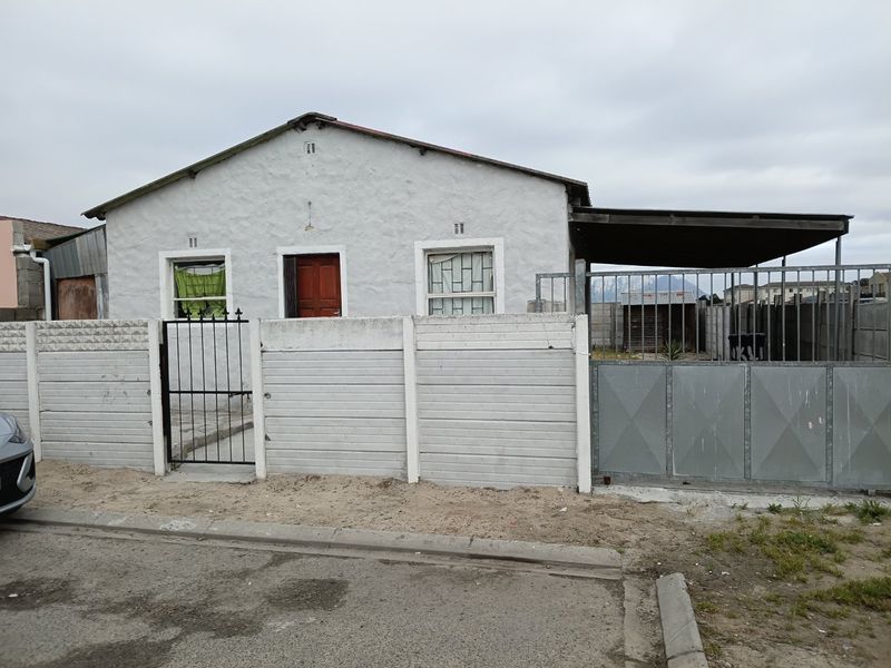 Front elevation of a single-story house featuring a precast concrete boundary wall, metal gates, and a covered carport area.
