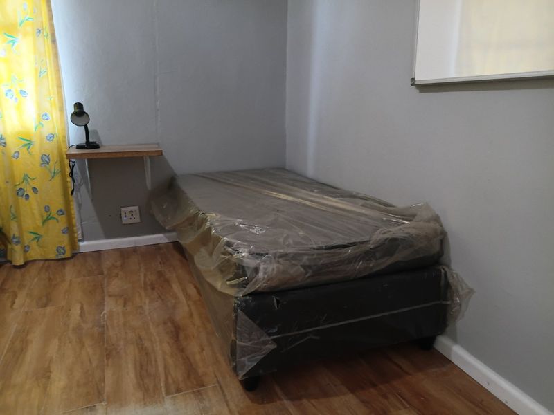 A simple bedroom featuring laminate flooring, a wall-mounted shelf, and neutral grey walls.