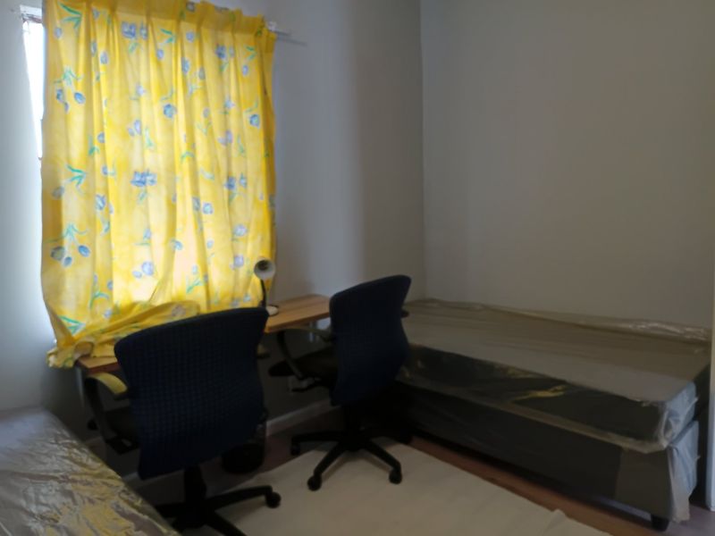 A simple bedroom space featuring a window with yellow curtains, suitable for use as a sleeping area or home office.