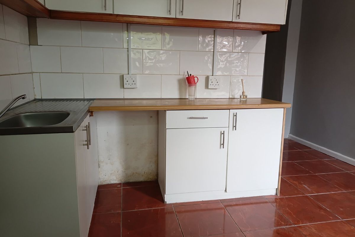 A functional kitchen area featuring white cabinetry, a laminate countertop, stainless steel sink, and tiled backsplash with ceramic floor tiles.