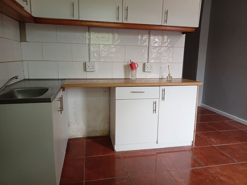 A functional kitchen area featuring white cabinetry, a laminate countertop, stainless steel sink, and tiled backsplash with ceramic floor tiles.
