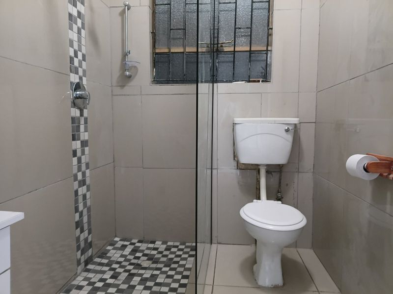 A functional bathroom featuring a shower with a glass screen, tiled finishes, and a standard toilet, requiring some cosmetic updates.
