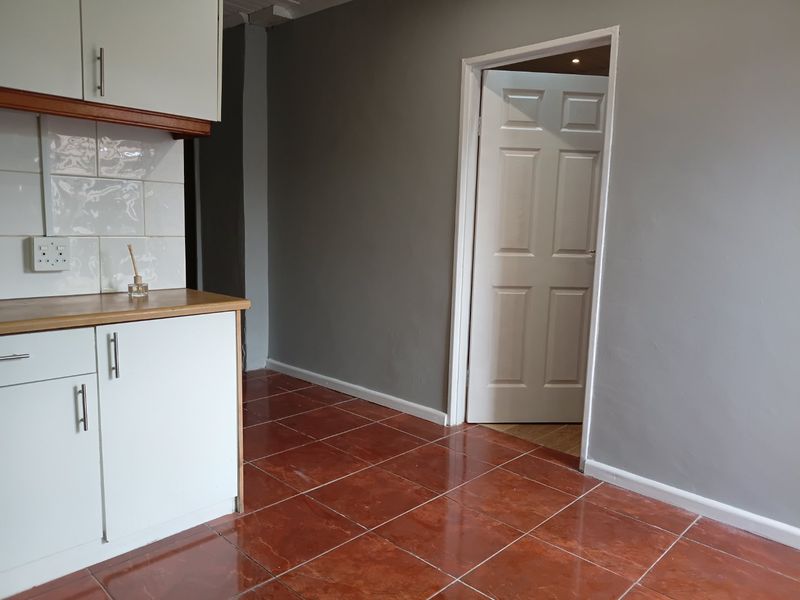 A functional kitchen area featuring white cabinetry, a tiled backsplash, and durable ceramic floor tiles, leading into an adjacent room through a panelled door.