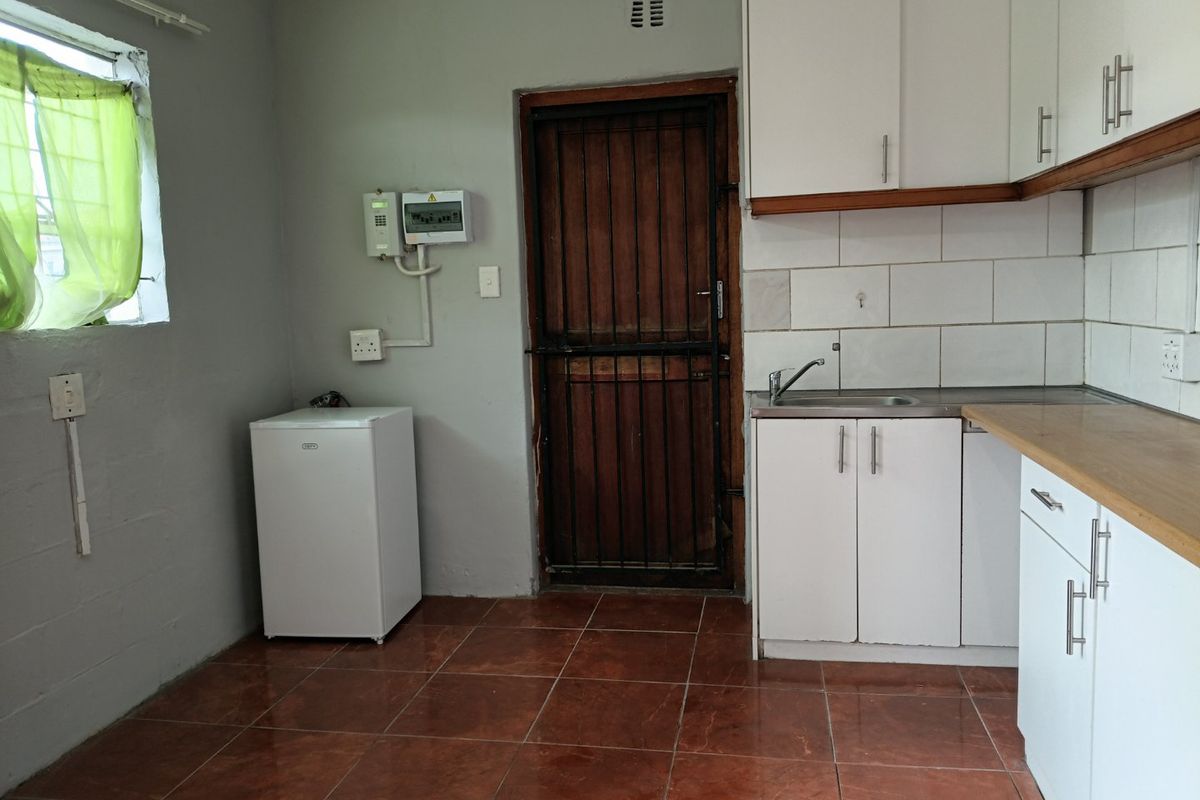 A functional kitchen area featuring white cabinetry, tiled flooring, a stainless steel sink, and a secure exterior door with a metal security gate.
