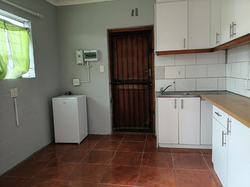 A functional kitchen area featuring white cabinetry, tiled flooring, a stainless steel sink, and a secure exterior door with a metal security gate.