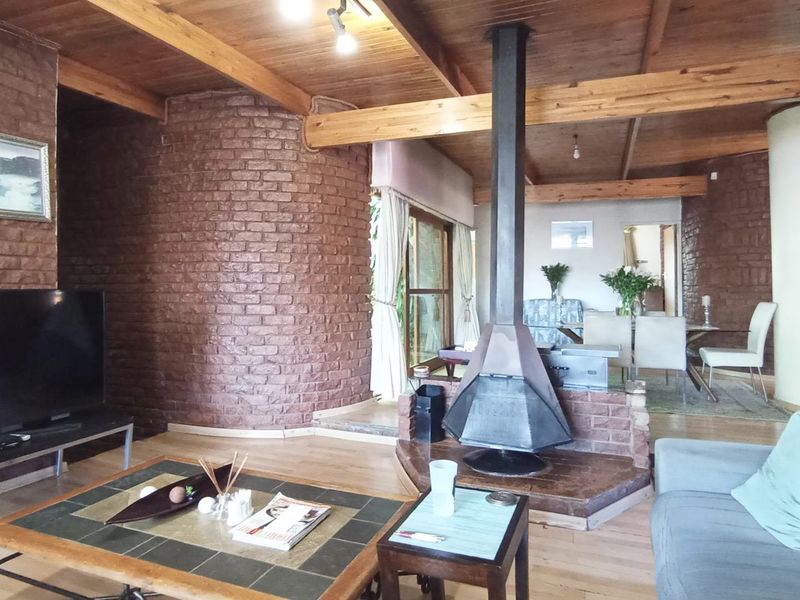 Spacious open-plan living area featuring exposed timber beams, rustic brick walls, and a central freestanding metal fireplace with timber flooring throughout.